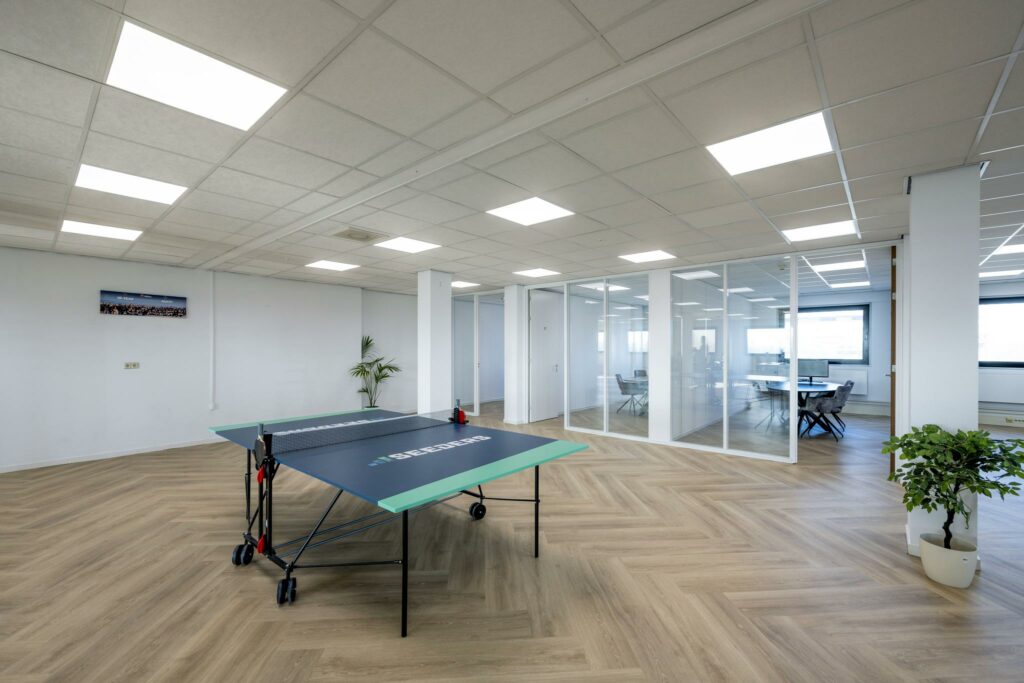 Moderne kantoorruimte aan de Joan Muyskenweg met glazen vergaderruimtes, een tafeltennistafel en houten visgraatvloer.